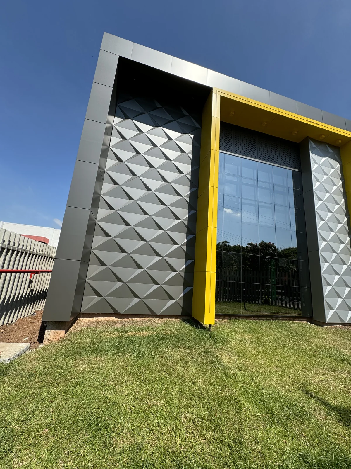 Corner of a building clad in dark and silver 3D ACM panels with a yellow frame