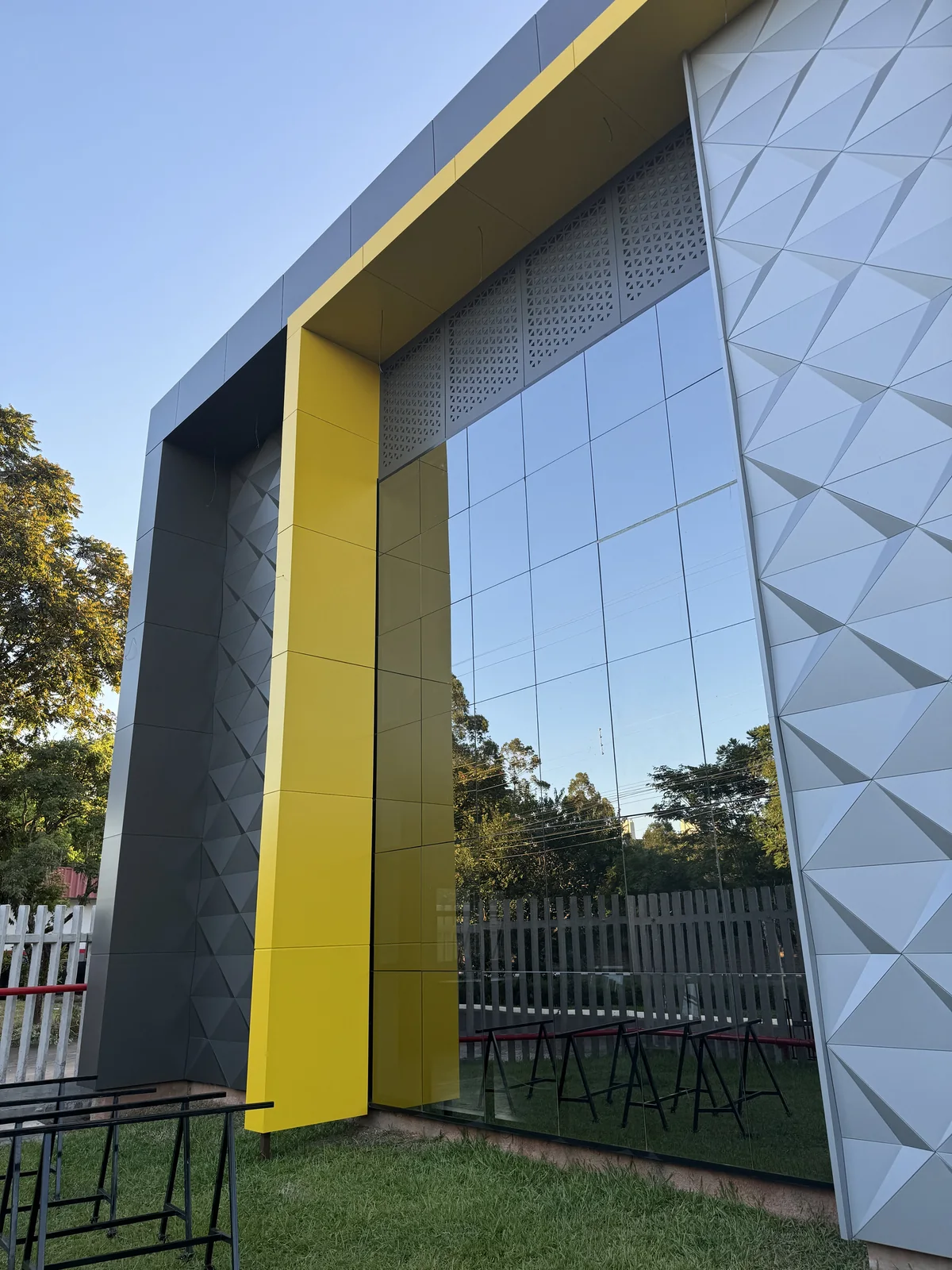 Tall silver 3D ACM panel column beside a glazed entrance with yellow ACM frame
