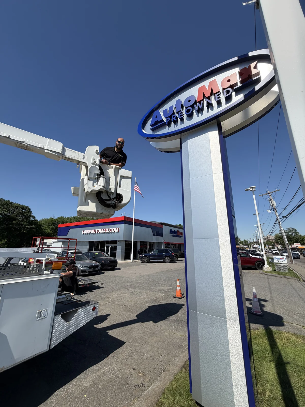 ACM-clad sign pylon with an oval Automax logo being installed with a bucket truck