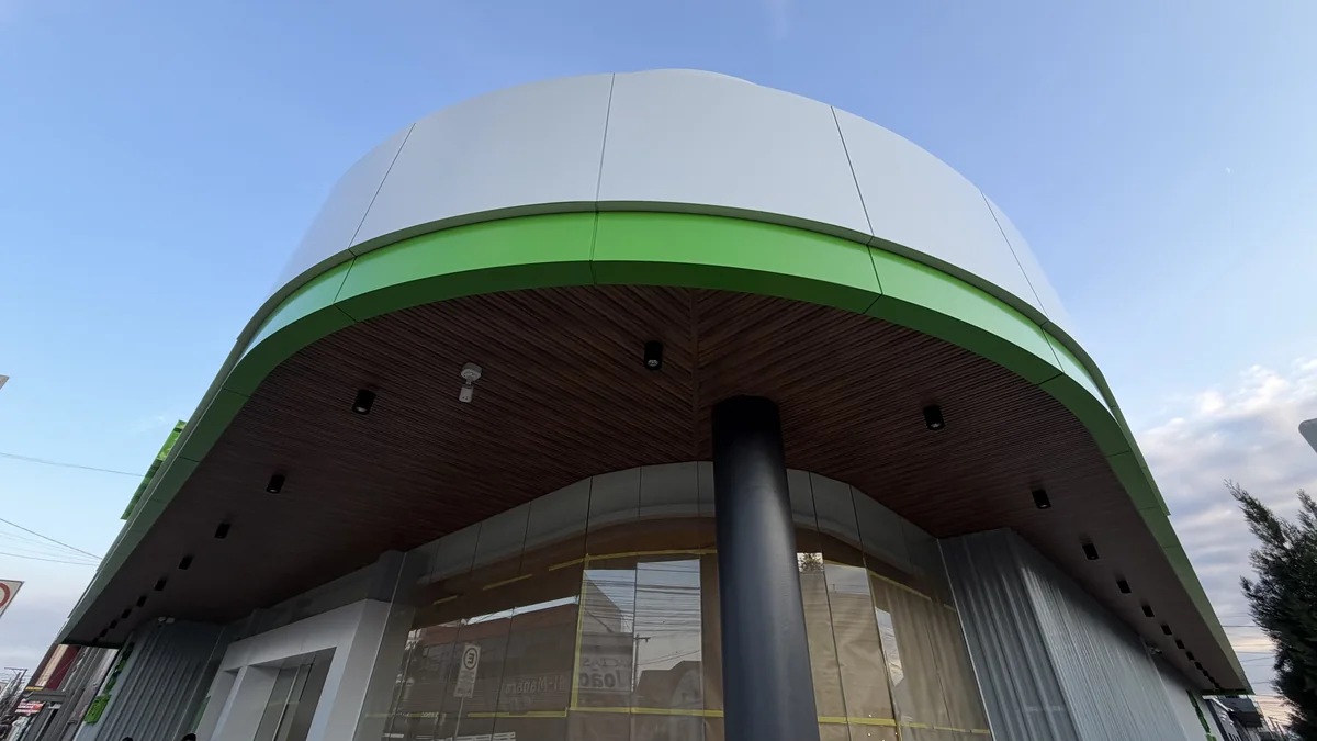Curved white ACM roof band with a green ACM stripe above a wood-look soffit and a round column