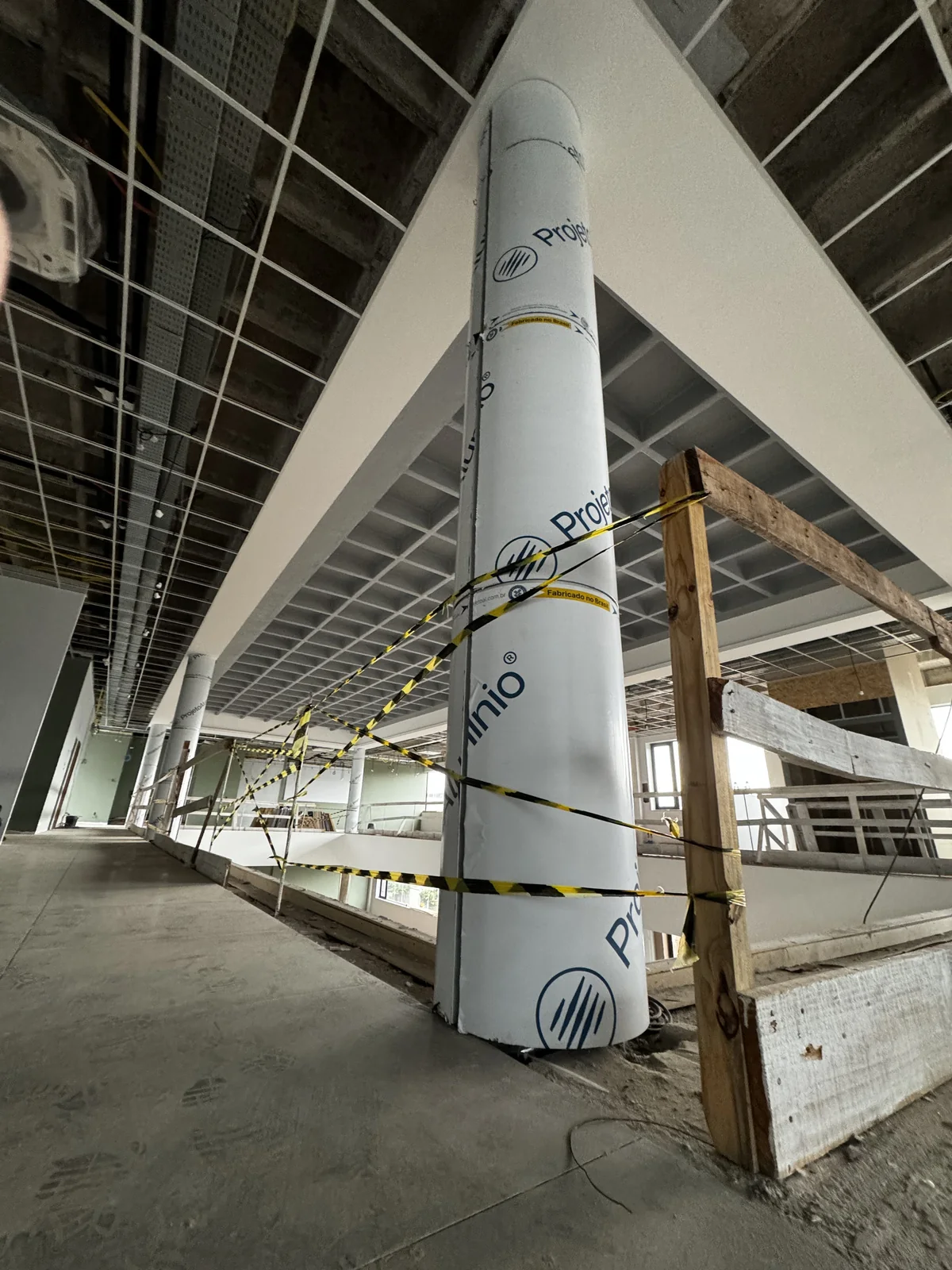 Round column wrapped in protective film inside a building under construction, beside a curved white ACM edge