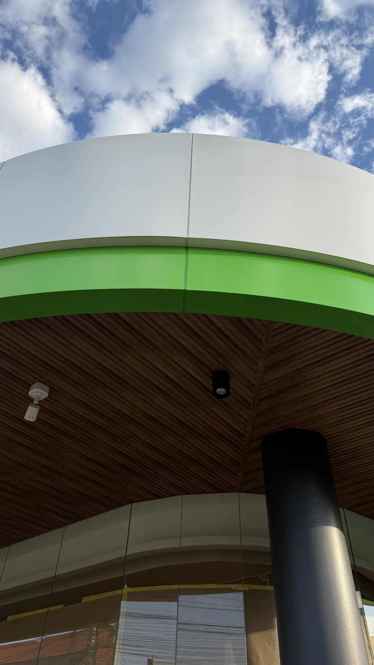 Curved ACM canopy edge with a green band against a cloudy sky