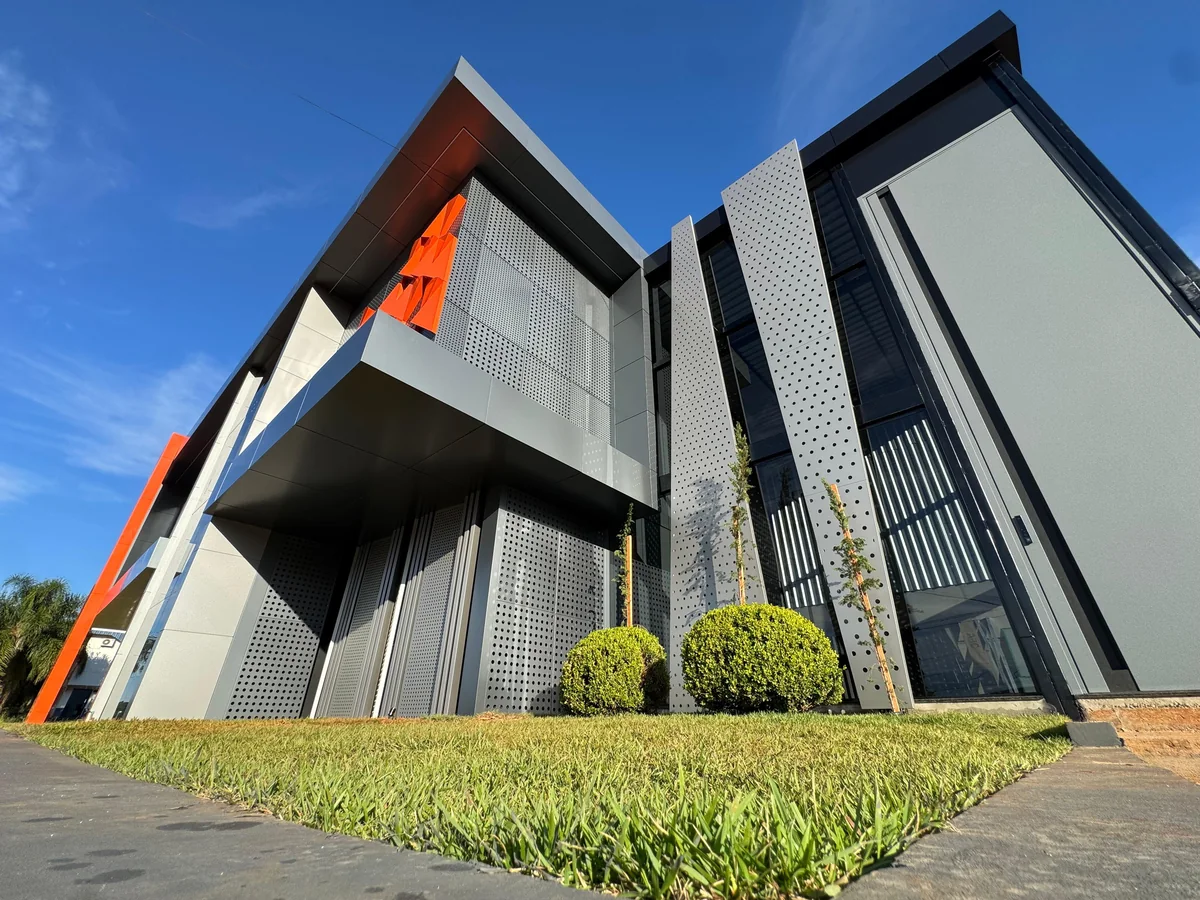 Building with perforated ACM fins and an orange accent, seen from the lawn