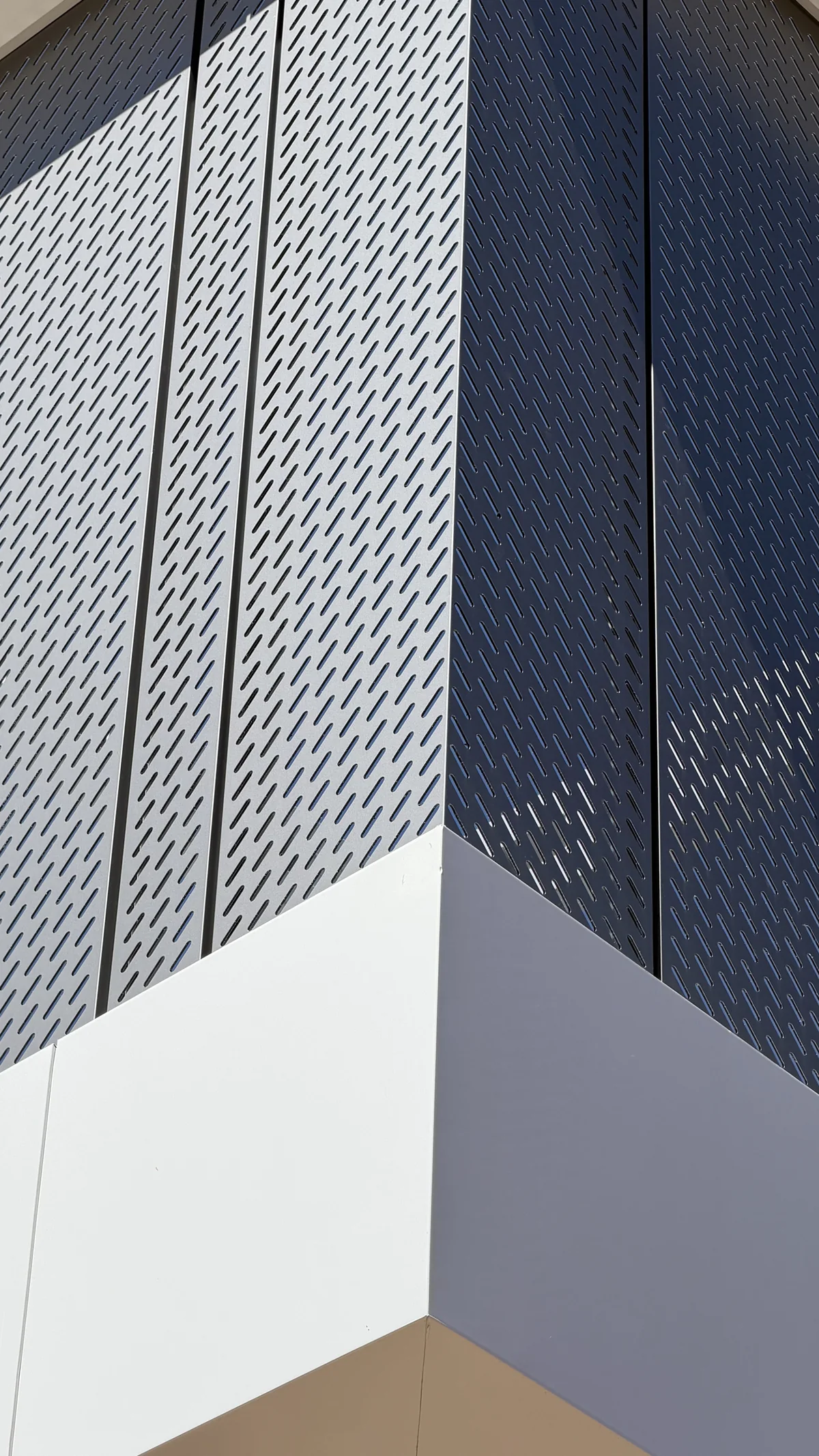 Corner of a facade with long slotted perforated ACM panels above a white ACM band