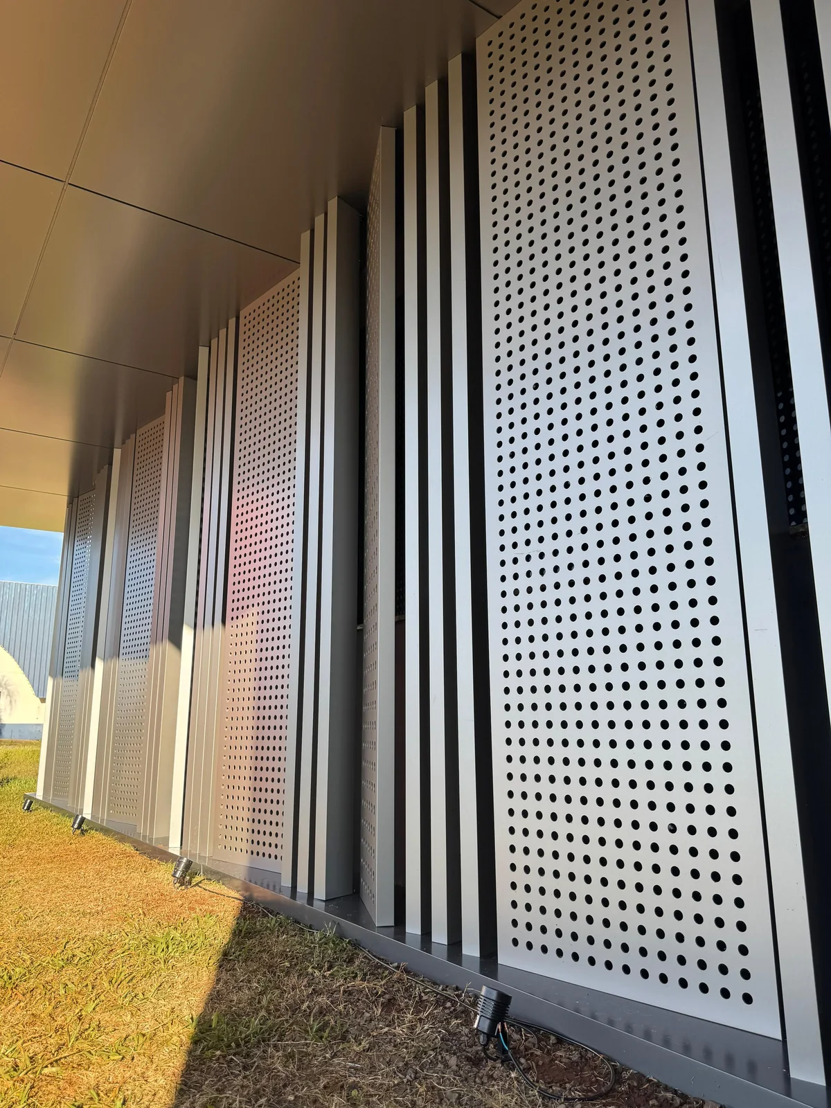 Tall perforated ACM panel with an even round-hole pattern beside vertical fins