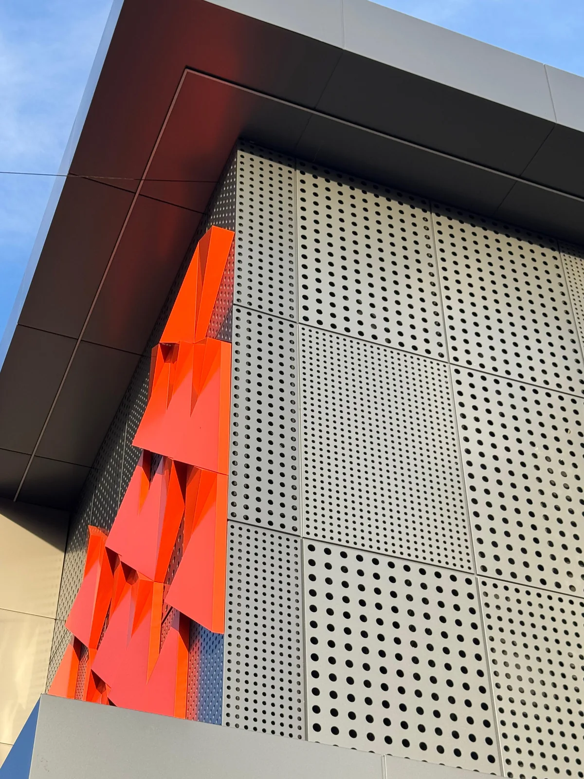 Perforated ACM panels meeting a dark soffit, with orange 3D accents